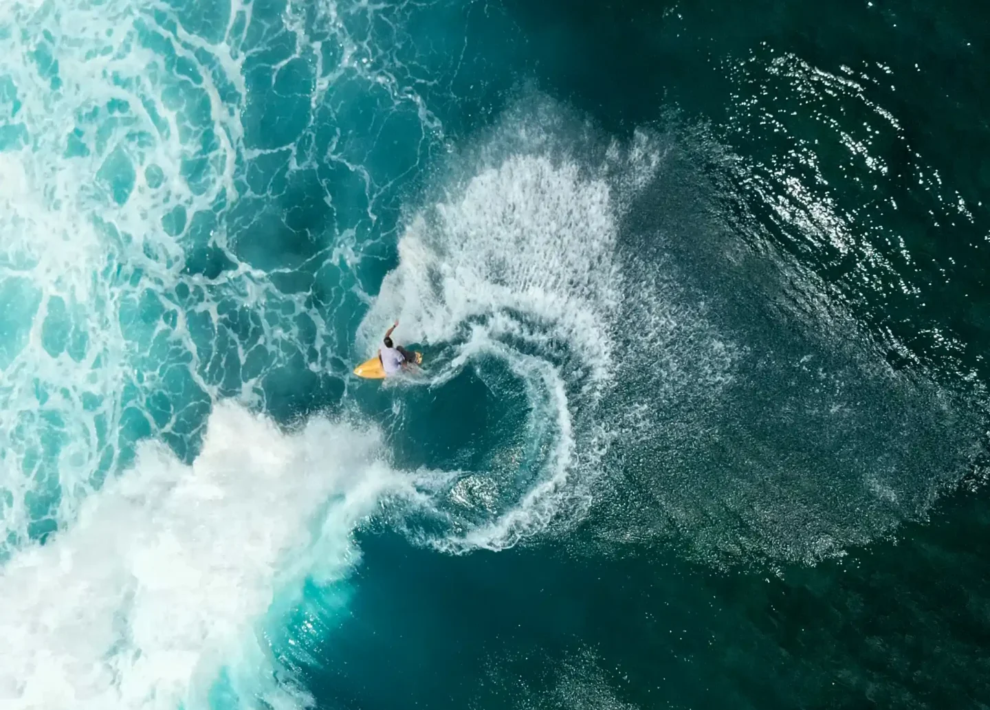 Aerial view of a surfer carving a turn on a turquoise ocean wave in Bali