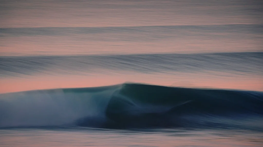 Artistic long-exposure photograph of a smooth ocean wave during a pastel sunset